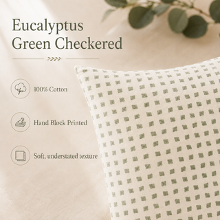 A close-up of a square throw pillow with a green and white checkered pattern, shown next to text describing its features: 'Eucalyptus Green Checkered', '100% Cotton', 'Hand Block Printed', and 'Soft, understated texture'.