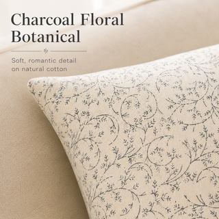 A close-up of a decorative throw pillow with a charcoal floral botanical pattern on a natural cotton fabric, styled on a beige sofa with text overlay reading 'Charcoal Floral Botanical'.