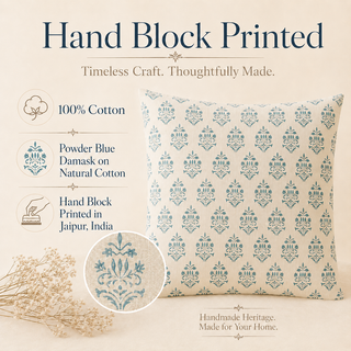 A decorative throw pillow with a hand block printed pattern, shown on a beige background with informational text and decorative dried flowers. The pillow features a cream base with a repeating dusty blue damask motif.