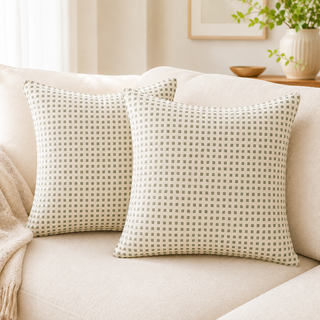 Two square throw pillows with a small beige and gray checkered pattern resting on a cream-colored sofa in a bright, modern living room.