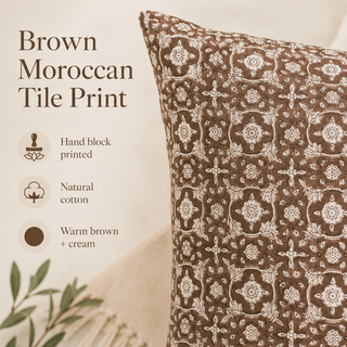 A close-up of a decorative throw pillow with a brown and cream Moroccan tile print, shown next to text describing the features: hand block printed, natural cotton, and warm brown + cream.