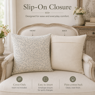 Two decorative throw pillows displayed on a vintage-style upholstered armchair in a softly styled room. One pillow has a light beige floral pattern, and the other is solid cream.