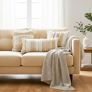 Beige sofa with patterned cushions and a blanket in a bright living room.