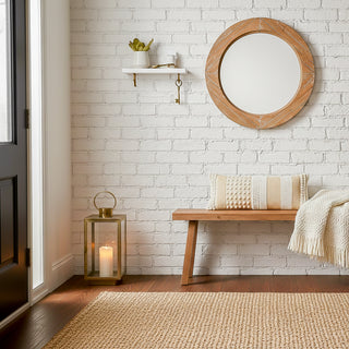 Nest living room with wooden bench, round mirror, and candle lantern against a white brick wall.