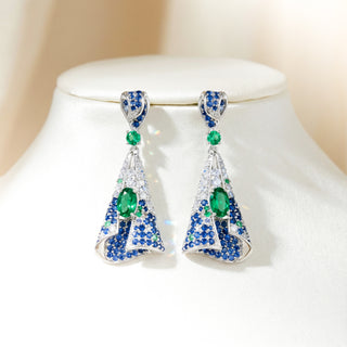 Pair of earrings with green and blue gemstones on a white stand.
